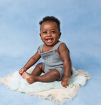 a smiling boy in a grey knitted outfit, sitting up against a blue backdrop for his little sitter baby photoshoot in aldershot, hampshire
