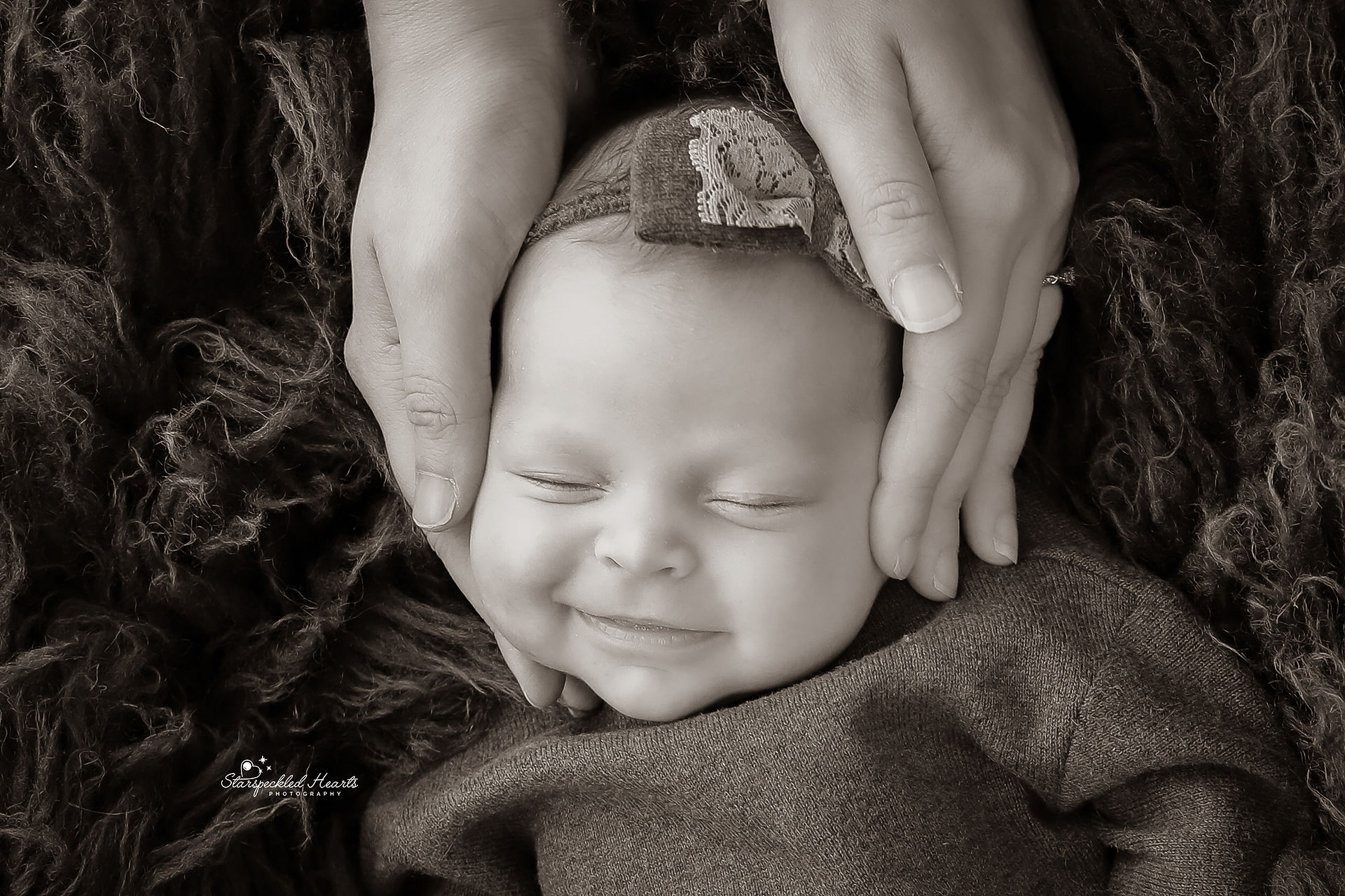 adorable smiling baby girl with her mothers hands placed on her cheeks in black and white