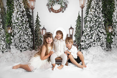 a Christmas themed background with green and white colours with three children sitting in the snow for their christmas photoshoot in aldershot, hampshire