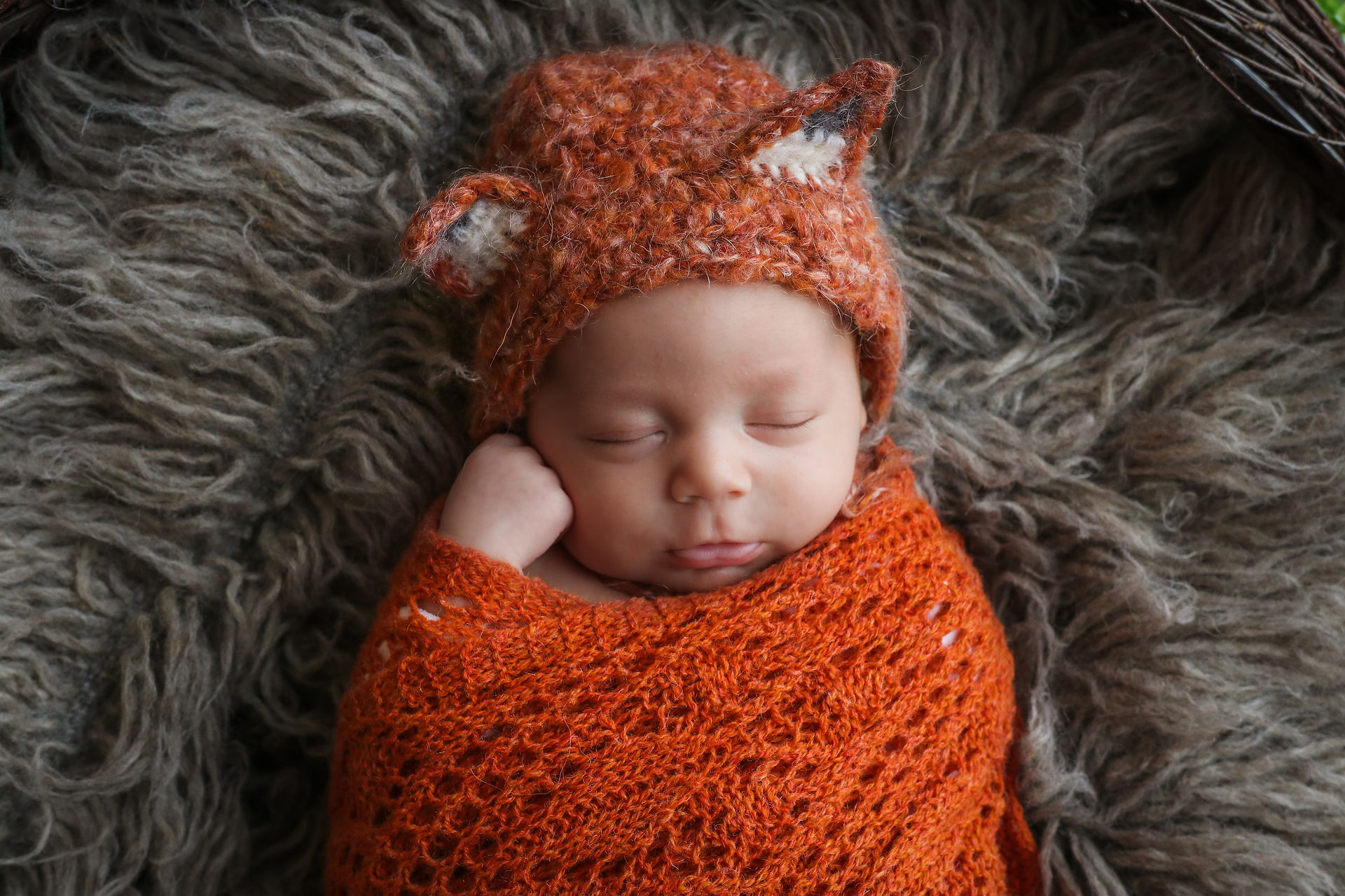 closeup of beautiful sleeping newborn wearing orange fox bonnet and wrap
