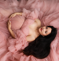 a maternity photo of a mum to be lying on a soft pink background holding her bump in a beautiful pink, flowy dress
