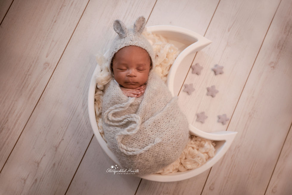 sleeping newborn wearing grey bunny bonnet laying in a crescent moon basket with little grey felt stars on a white wooden floor for his newborn photography session in aldershot hampshire