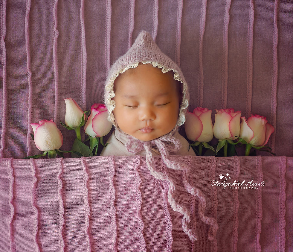 baby girl wearing a pink embroidered bonnet, laying next to roses