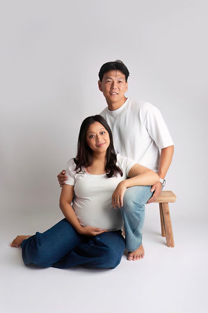 Expectant couple during a natural studio maternity photoshoot in Hampshire by Starspeckled Hearts Photography, with mum seated on the floor cradling her baby bump while dad sits behind.