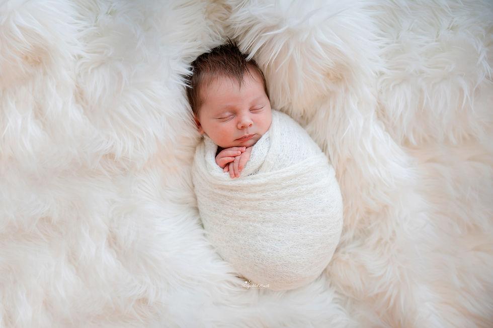 cute sleeping newborn baby boy swaddled in white with his hands folded