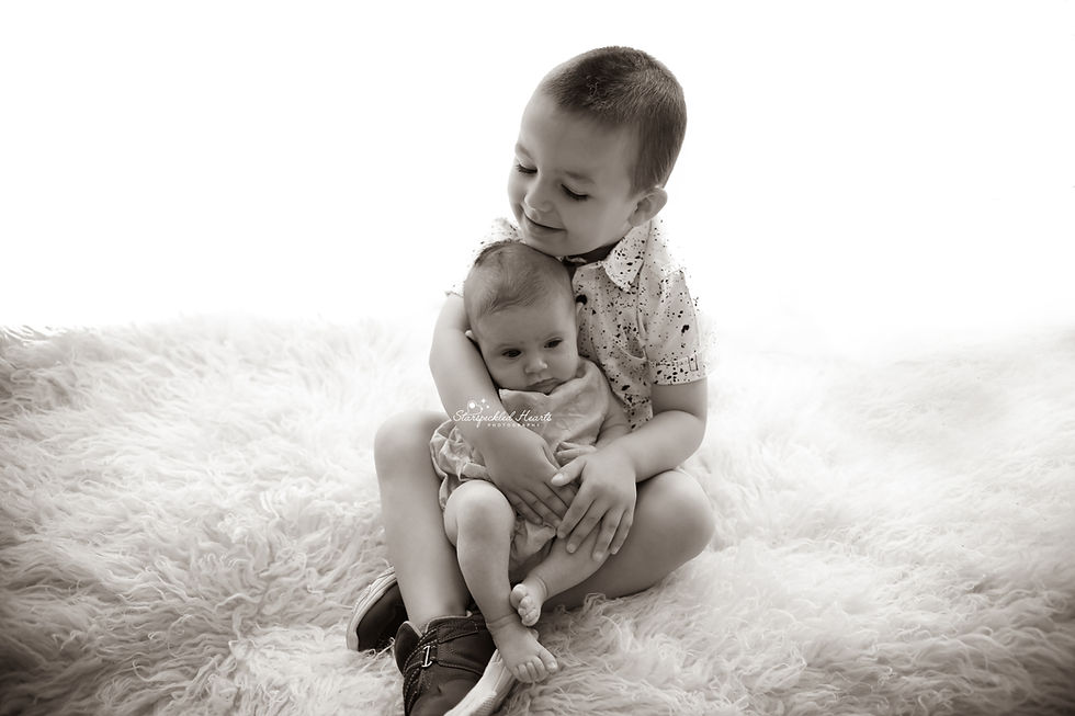 baby boy sitting on a white fluffy rug, holding his baby sister