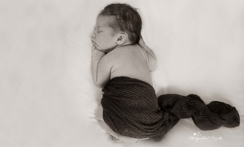 black and white photo of a sleeping baby boy, seen from above, wrapped in a dark cheesecloth