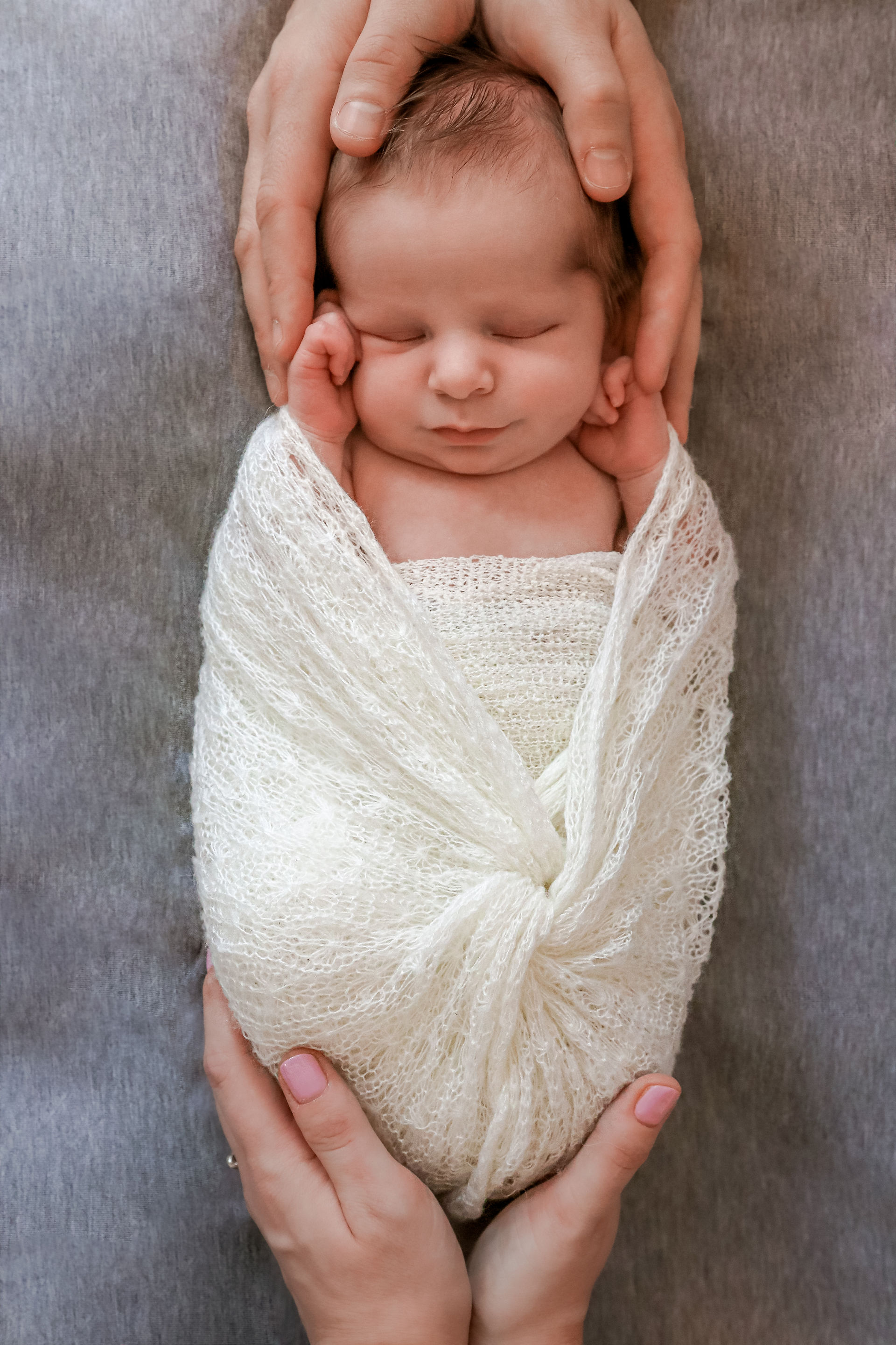 newborn held by two pairs of hands