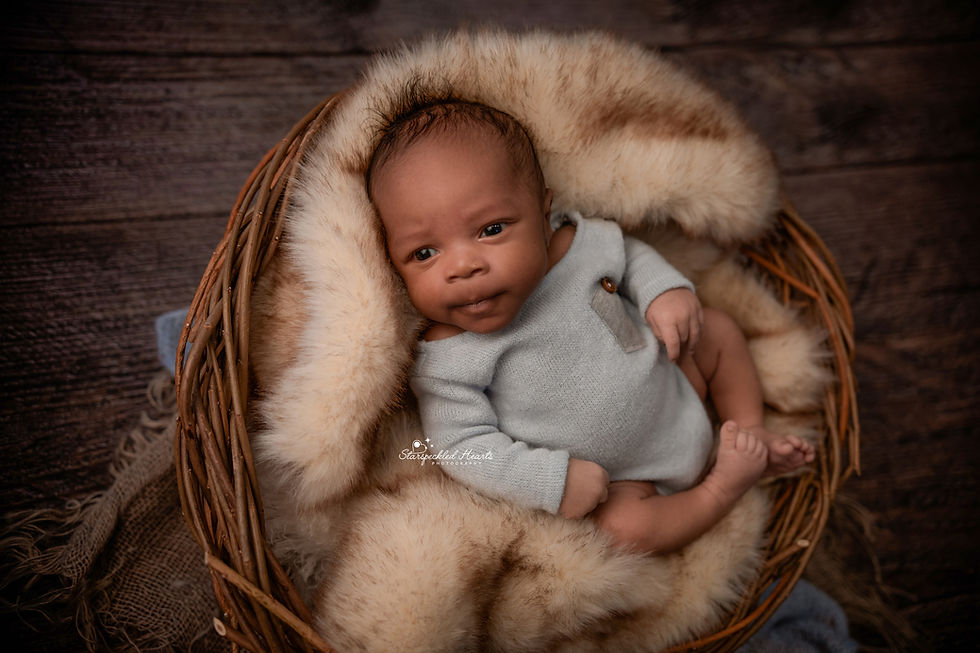 newborn with big brown eyes wearing a baby blue romper lying in basket stuffed with a brown fur blanket for his newborn photography session in aldershot hampshire berkshire surrey