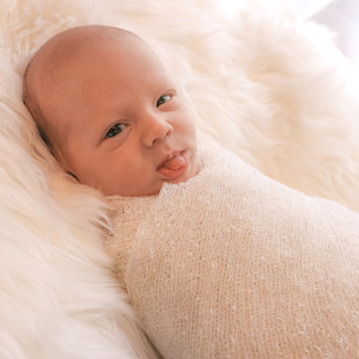 newborn wearing white sticking out tongue