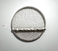 Œuvre murale circulaire et texturée de l'artiste Marie-Josée Gustave, composée de motifs entrelacés en matériaux naturels. Vue d'installation en galerie. Exposition "Couples Artistes" (2024), Fondation Jordi Bonet, Art contemporain. Commissaire : Laurent Bonet. / Circular and textured wall-mounted artwork by artist Marie-Josée Gustave, composed of interlaced patterns in natural materials. Gallery installation view. "Couples Artistes" exhibition (2024), Fondation Jordi Bonet, Contemporary Art. Curator: Laurent Bonet.