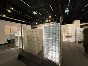 Détail de la scénographie montrant un réfrigérateur évidé, spectre de notre surconsommation, isolé derrière une clôture métallique. Ce dispositif scénographique n'est pas un lieu de vente mais un simulacre interrogeant notre compulsion à remplir l'espace pour anesthésier l'angoisse du vide. Projet « Horror Vacui » (2028-2030), Fondation Jordi Bonet, Art contemporain. Commissaire : Laurent Bonet. / Detail of the scenography showing a gutted refrigerator, a spectre of our overconsumption, isolated behind a metal fence. This scenographic device is not a retail space but a simulacrum questioning our compulsion to fill space to numb the anxiety of the void. "Horror Vacui" project (2028-2030), Fondation Jordi Bonet, Contemporary Art. Curator: Laurent Bonet