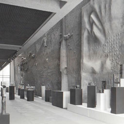 Vue d'installation d'archives en noir et blanc dans le vaste hall du Grand Théâtre de Québec, présentant de multiples sculptures en bronze et céramique de Jordi Bonet sur socles. En arrière-plan, l'immense murale texturée en béton de l'artiste domine l'espace architectural baigné de lumière naturelle. Fondation Jordi Bonet, Art contemporain. Commissaire : Laurent Bonet. / Black and white archival installation view in the vast hall of the Grand Théâtre de Québec, presenting multiple bronze and ceramic sculptures by Jordi Bonet on pedestals. In the background, the artist's massive textured concrete mural dominates the architectural space bathed in natural light. Fondation Jordi Bonet, Contemporary Art. Curator: Laurent Bonet.