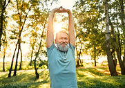 Smiling senior man stretching his arms overhead outdoors, free of back pain after spine surgery abroad