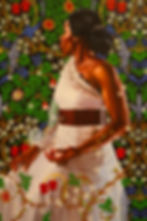 A woman in a white dress with a brown belt poses against a vibrant floral-patterned backdrop, exuding elegance and serenity.