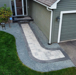 Front-entry paver walkway with contrasting border stones, gravel accents, and driveway connection from Anderson Bros Outdoors.