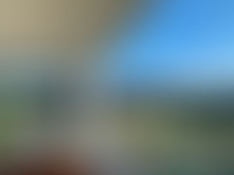 A covered deck showing soft outdoor furniture, with a glass fence overlooking gardens, with mountains and blue sky in the background.