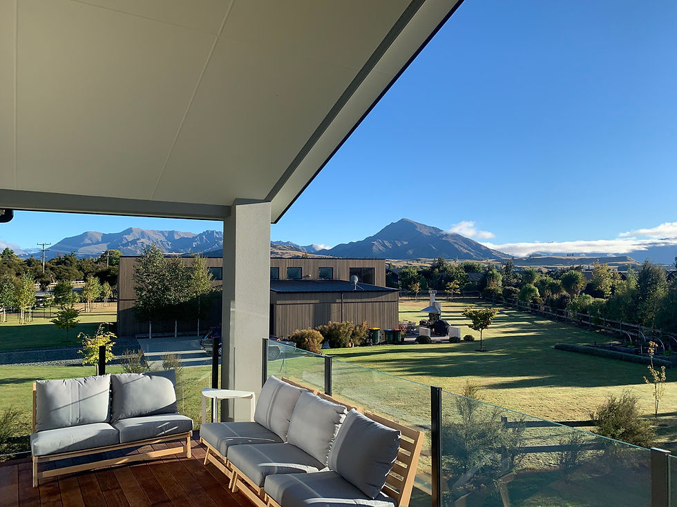 Modern patio with gray sofas overlooks a spacious garden with distant mountains. Clear blue sky enhances the tranquil atmosphere.