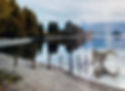 A tranquil lake with still water reflects trees and mountains. A sandy shore with a fence stretches along the water. The mood is peaceful.