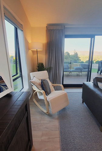 The indoor/outdoor flow for the upstairs. A rocking chair and buffet cabinet. The area shows art and a floor lamp, plus a view of the outdoor deck.