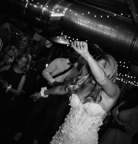 Frau in Brautkleid tanzt ausgelassen auf einer Party mit Lichtern im Hintergrund.