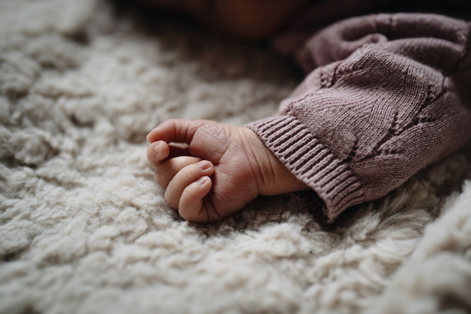 Kleine Babyhand im rosa Strickärmel auf weicher Decke liegend.