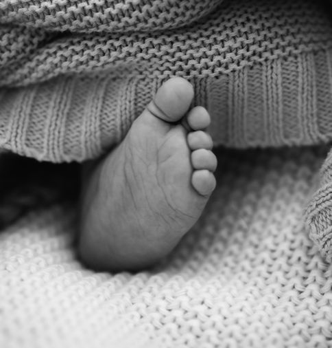 Nahaufnahme eines zarten Babyfußes unter einer weichen Strickdecke, schwarz-weiß.