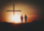 Silhouette of two young men walking towards a cross in a sunset