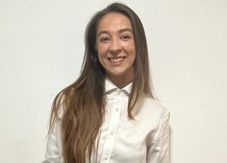 Woman in white shirt smiles against a plain white background. Her long hair is down. The image conveys a cheerful mood.
