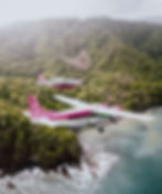 Two small airplanes flying over jungle and ocean