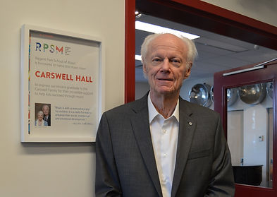 A well-dressed man stands confidently before a sign, exuding professionalism and authority.