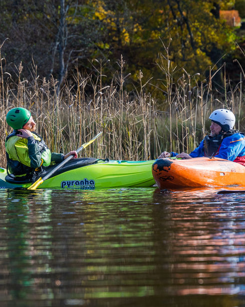 Två paddlare i kajaker sitter bredvid varandra på lugnt vatten och pratar under träning.