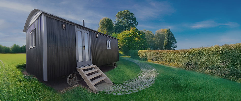 The Bantham shepherd’s hut with steps and wheels, set beside a cobbled path in a peaceful UK countryside location, surrounded by green hedges and trees.