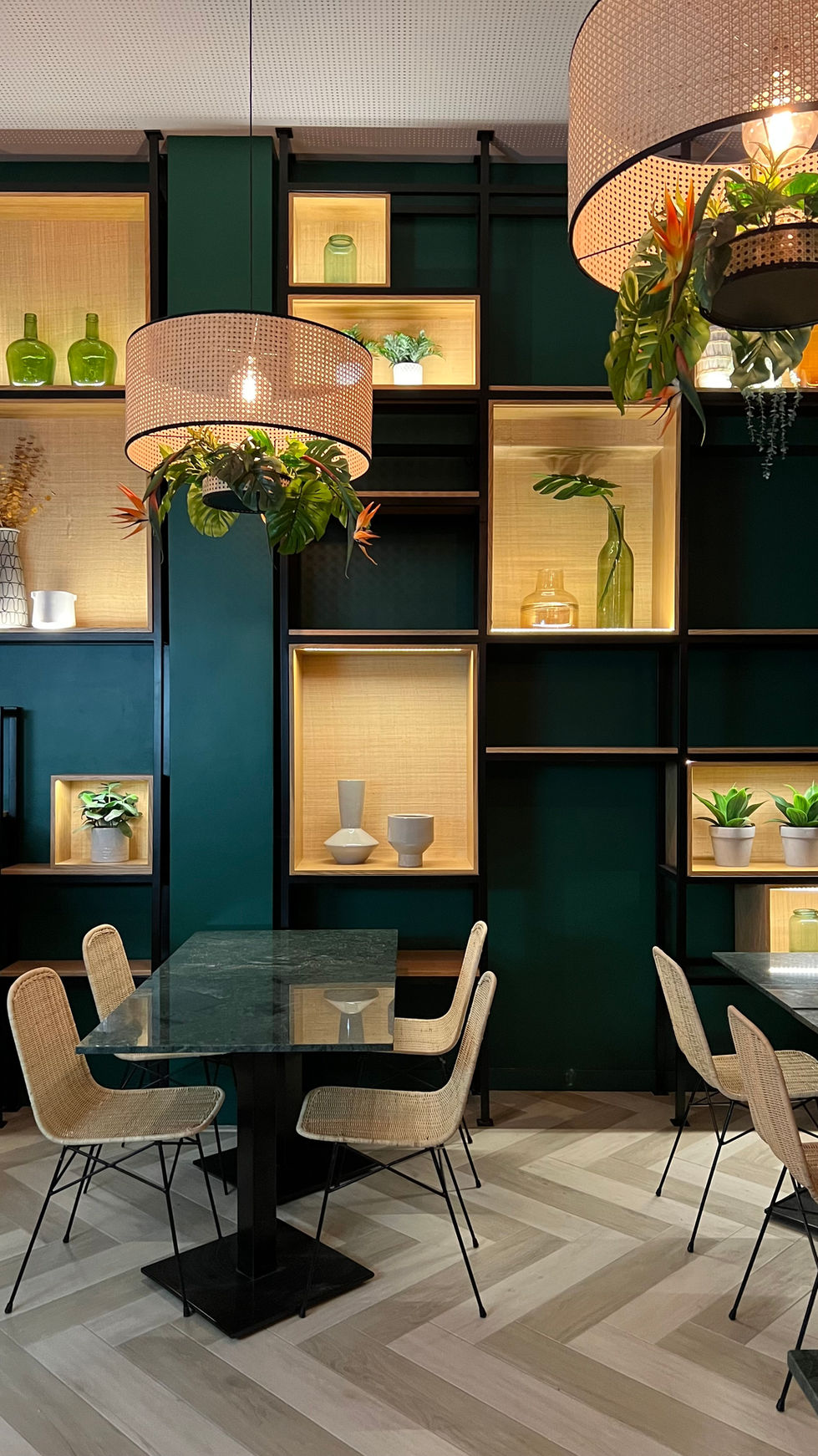 restaurante em tons de verde escuro, vegetação nos candeeiros suspensos, estante de parede com jarras