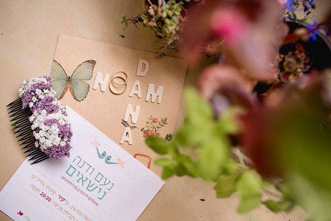 הזמנה וטבעות הזוג מצולמים מבעד לפרחים מלמעלה