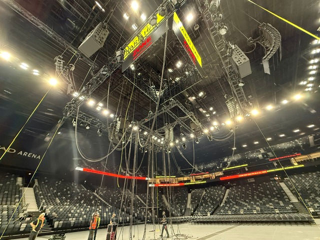 Following the arena pre-rig with rigging points, motors and cables hanging above the floor, lighting and audio are up.