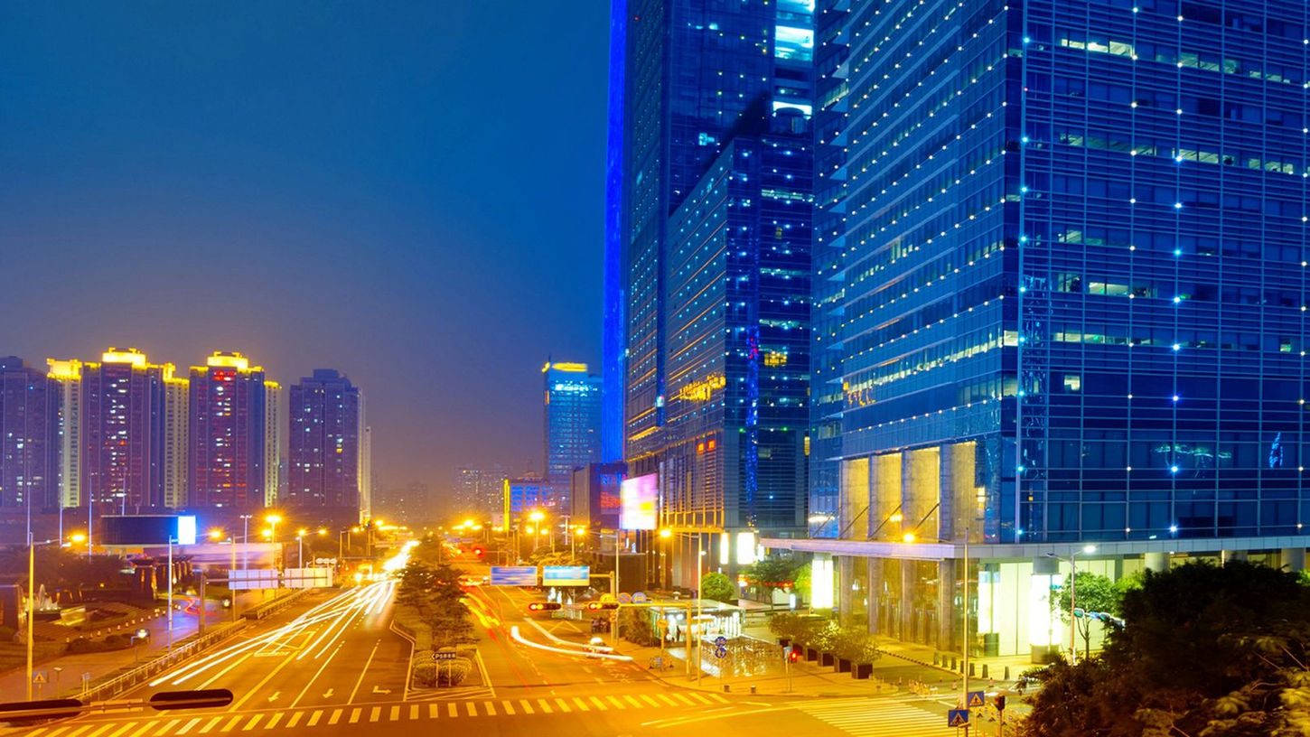 Paisagem urbana noturna, edifícios modernos e rastros de luz.