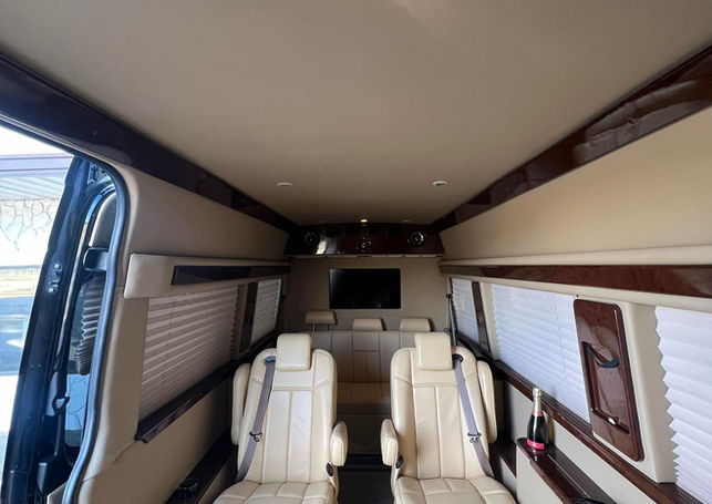 A luxury van interior with cream leather captain chairs facing each other and wood trim.