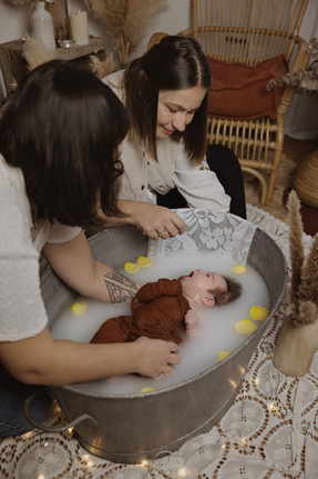 Bébé dans un bain de lait enveloppé avec ses 2 mamans qui lui donnent le bain