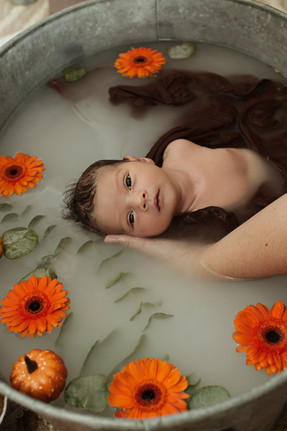 Bébé dans un bain de lait avec des fleurs oranges et du feuillage dans le bain