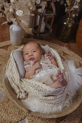 bébé dans un contenant en bois habillée d'une robe bohème et entourée de tissus en dentelle