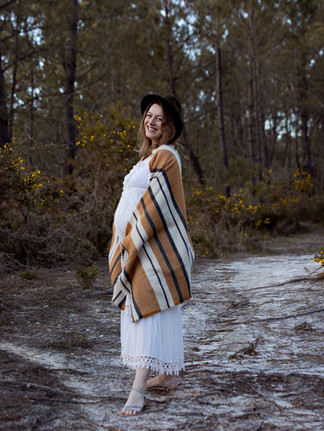 femme enceinte avec un grand sourire qui pose avec son ventre rond dans la forêt
