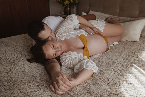 Couple complice allongé sur un lit, homme embrassant le ventre rond de sa compagne, séance grossesse intimiste Bordeaux