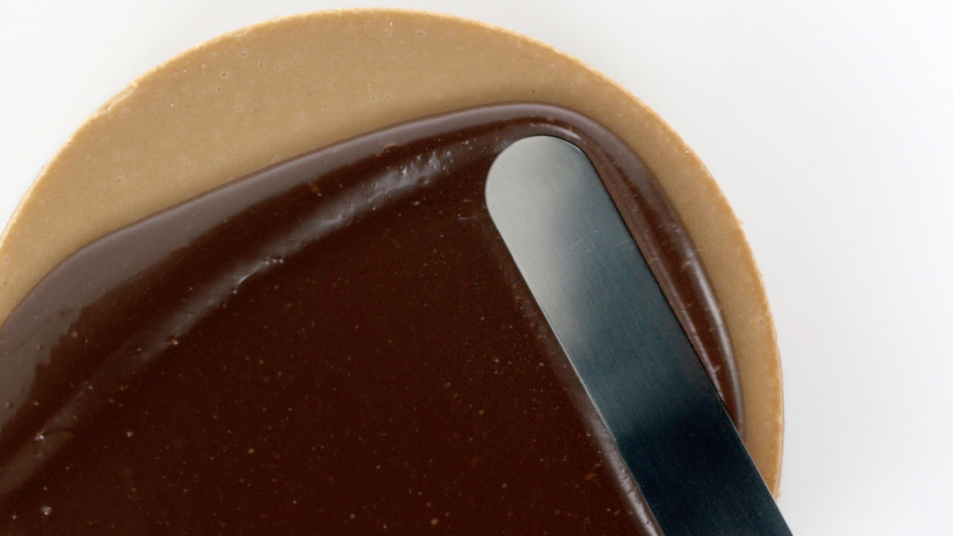 Une spatule étale du chocolat sur un gâteau.