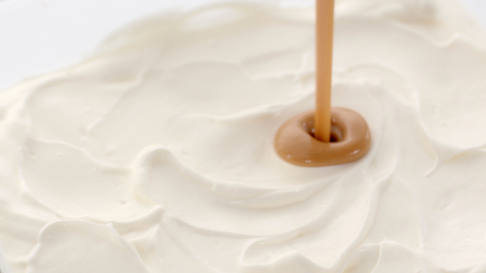 Un coulis de caramel pénètre une crème blanche.