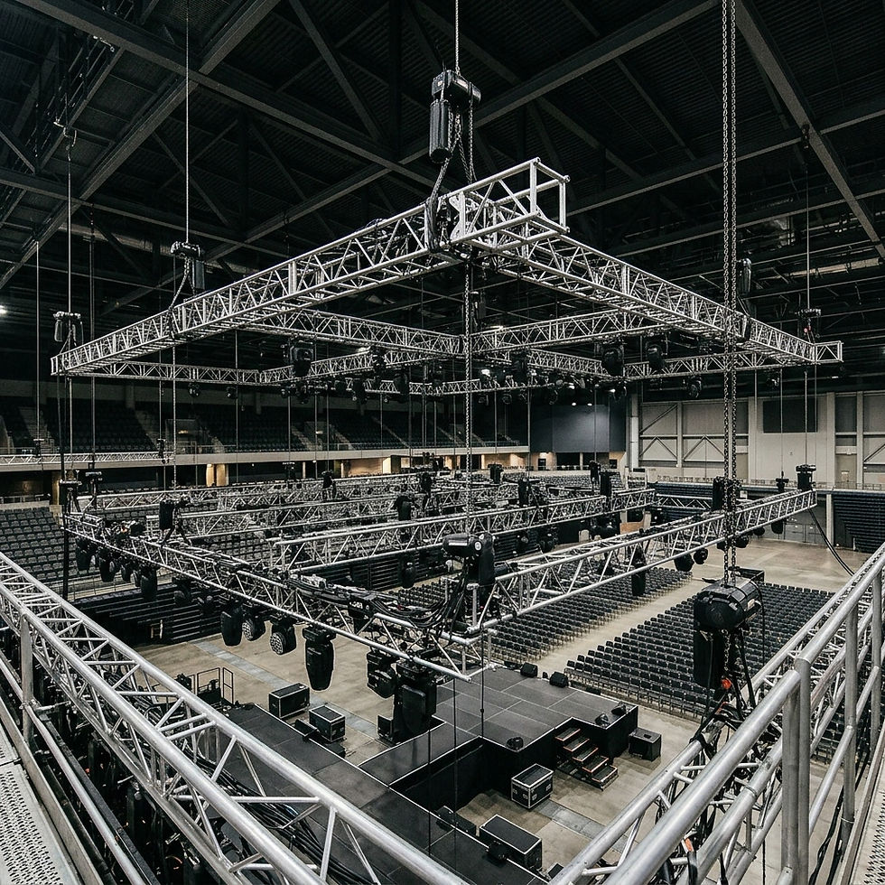 Empty indoor arena with suspended silver lighting truss rigs over a stage and rows of seats