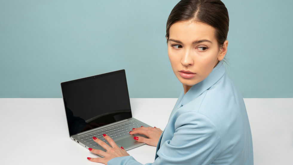 Woman on laptop looking over her shoulder unsure