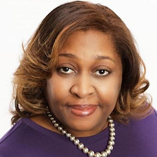 Board Member Joy Goodner. She is a black woman with short brown hair and is wearing a string of pearls and a purple blouse.