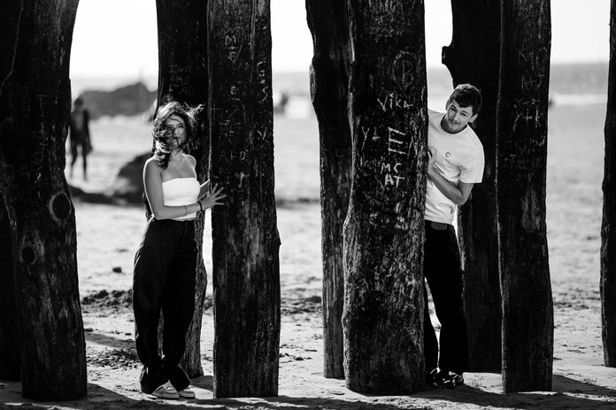 Jeune couple pose au milieu des poteaux en bois qui servent à casser les vagues sur la plage