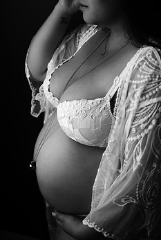 Gros plan de profil sur le ventre rond d'une femme enceinte portant un soutien-gorge blanc brodé et un kimono en dentelle.